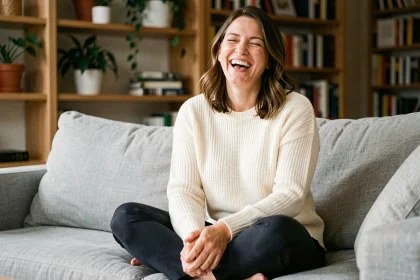 Femme souriante assise sur un canapé en lin gris, illustrant les bienfaits du rire sur la santé immunitaire